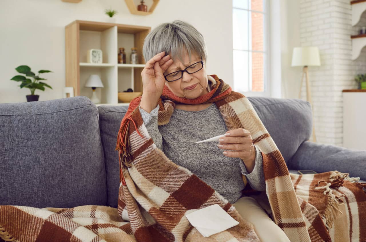 Elderly lady at home sitting on sofa wrapped up warm